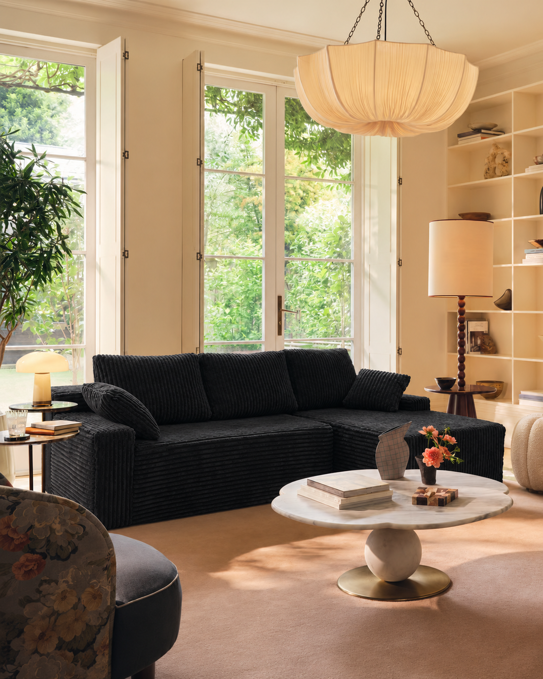 Black L-shaped couch with an accent chair in a sunlit room with wood flooring